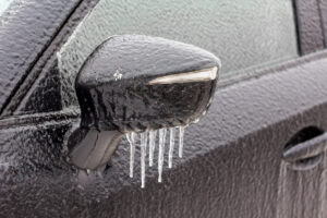 The car was iced over in winter after an icy rain. car mirror with icicles, covered with ice. Frost, rain and a car. Blurred background.
